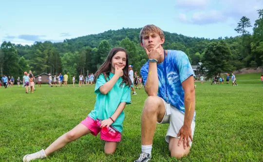 One kid and one camp counselor kneel on a field doing funny faces for the camera. 