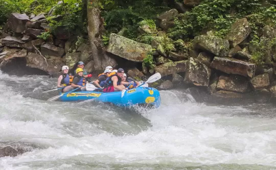 A group of kids in blue raft going over a white water rapid 
