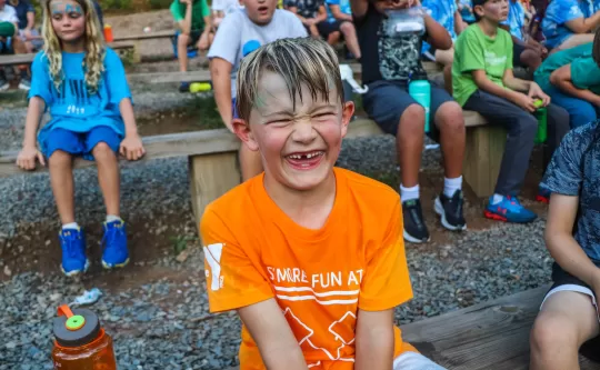 Young boy smiles big for the camera, several children are in the background.