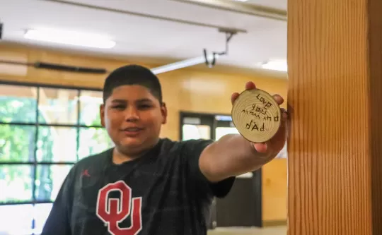Child holding up a circular wood craft that he has burned "love you mom and dad" on it