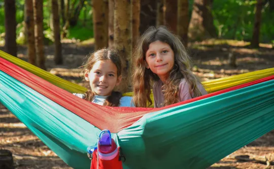 Two girls sit together in a hammock at Hammockville.